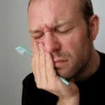 Man Holds Side Of Mouth With Pain - Trade Winds Dental