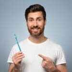 Man Smiling And Holding A Toothbrush He Is Pointing At - Trade Winds Dental