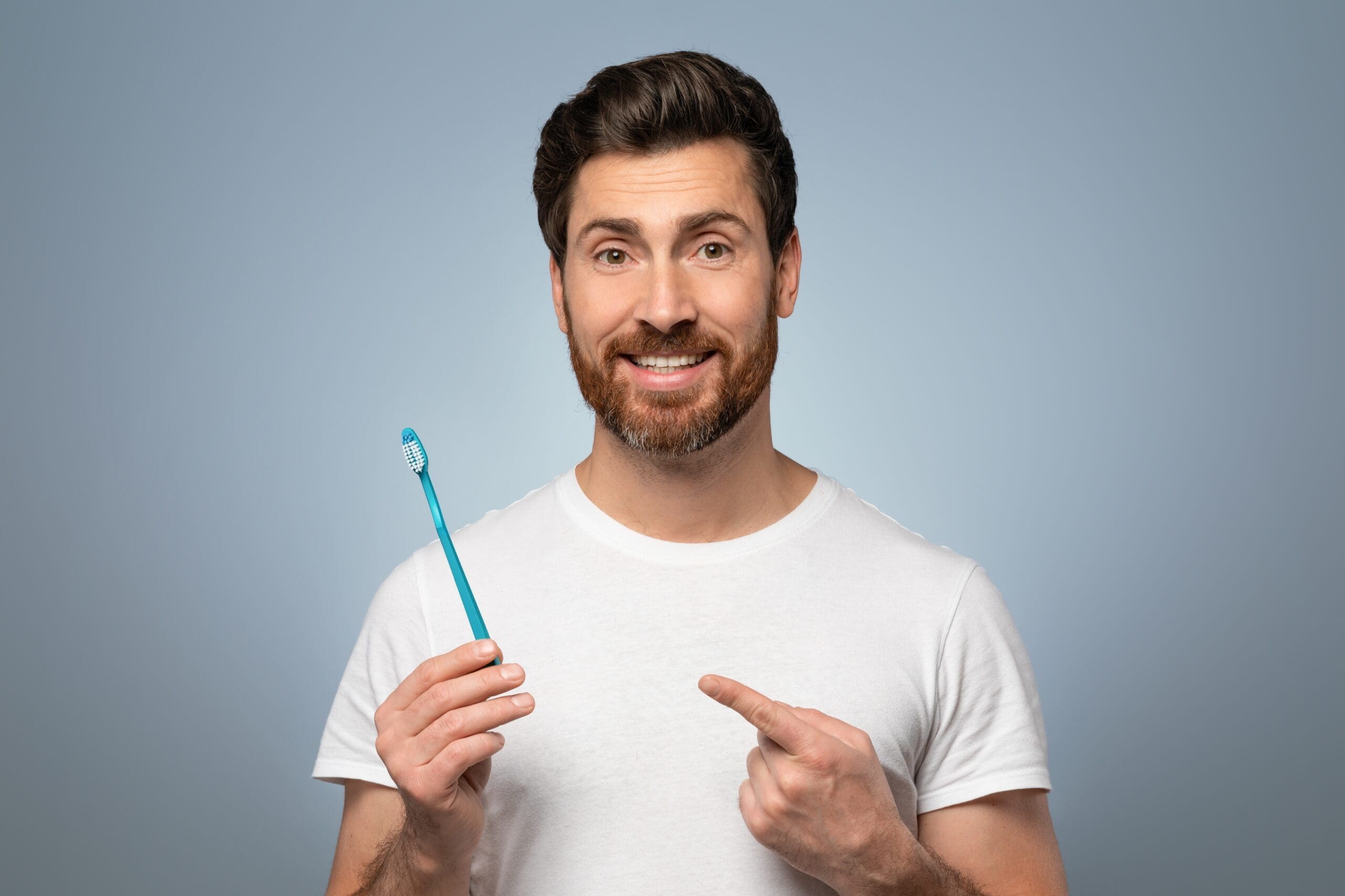Man Smiling And Holding A Toothbrush He Is Pointing At - Trade Winds Dental