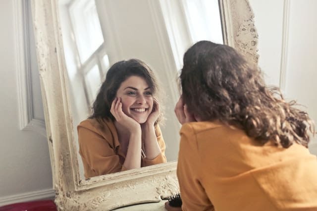 Woman Smiles In Mirror - Trade Winds Dental