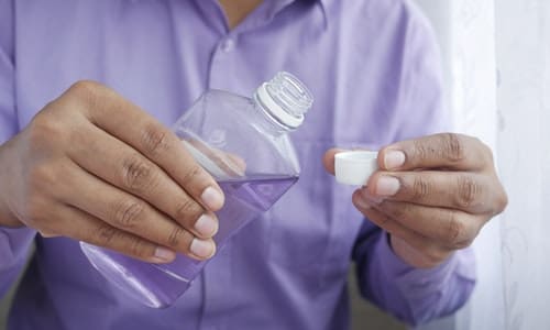 Person Pouring Mouthwash In Cup - Trade Winds Dental