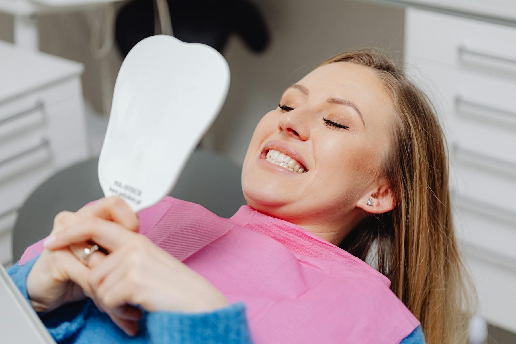 Dental Patient Holds Mirror And Checks Teeth With Smile - Trade Winds Dental