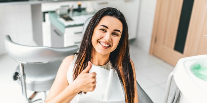 Smiling woman giving a thumbs-up in a dental chair.